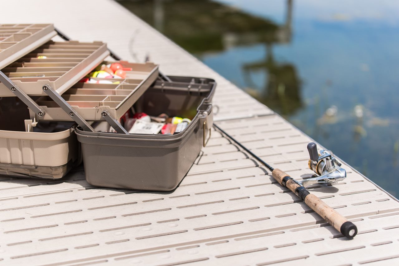 A fishing pole and tackle box sitting on Titan Classic on a dock over a lake.