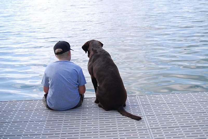 A young boy is fishing in a lake with his brown dog next to him sitting on a Titan Deck marine deck.