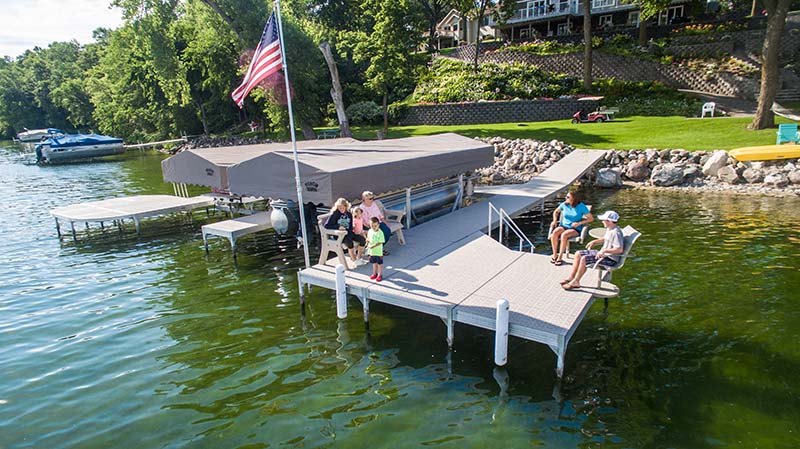 A family relaxes on a marine deck with Titan Deck propylene plastic material. There’s an American flag waving and a lush green lawn in the back.