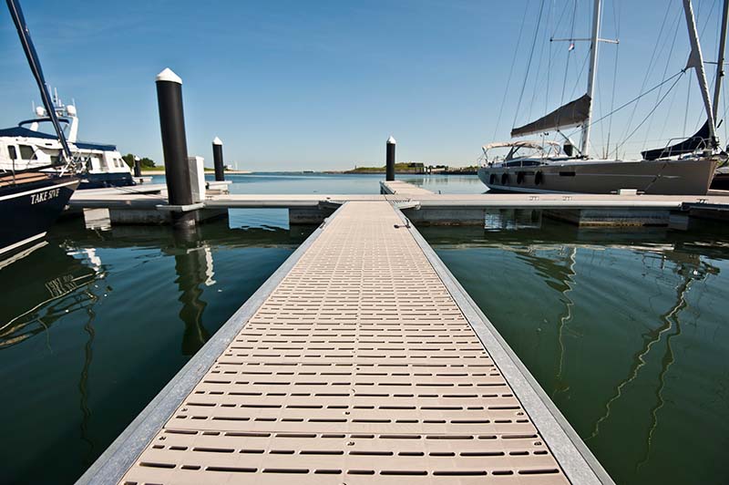A view down a tan dock on top of the water. A sailboat is seen docked in the background. 
