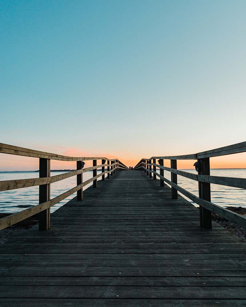 The view down a wooden pier over the water at sunset.
