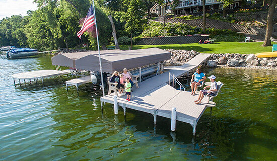 A family relaxing on a dock with titan decking. An American flag is blowing in the wind over the lake.