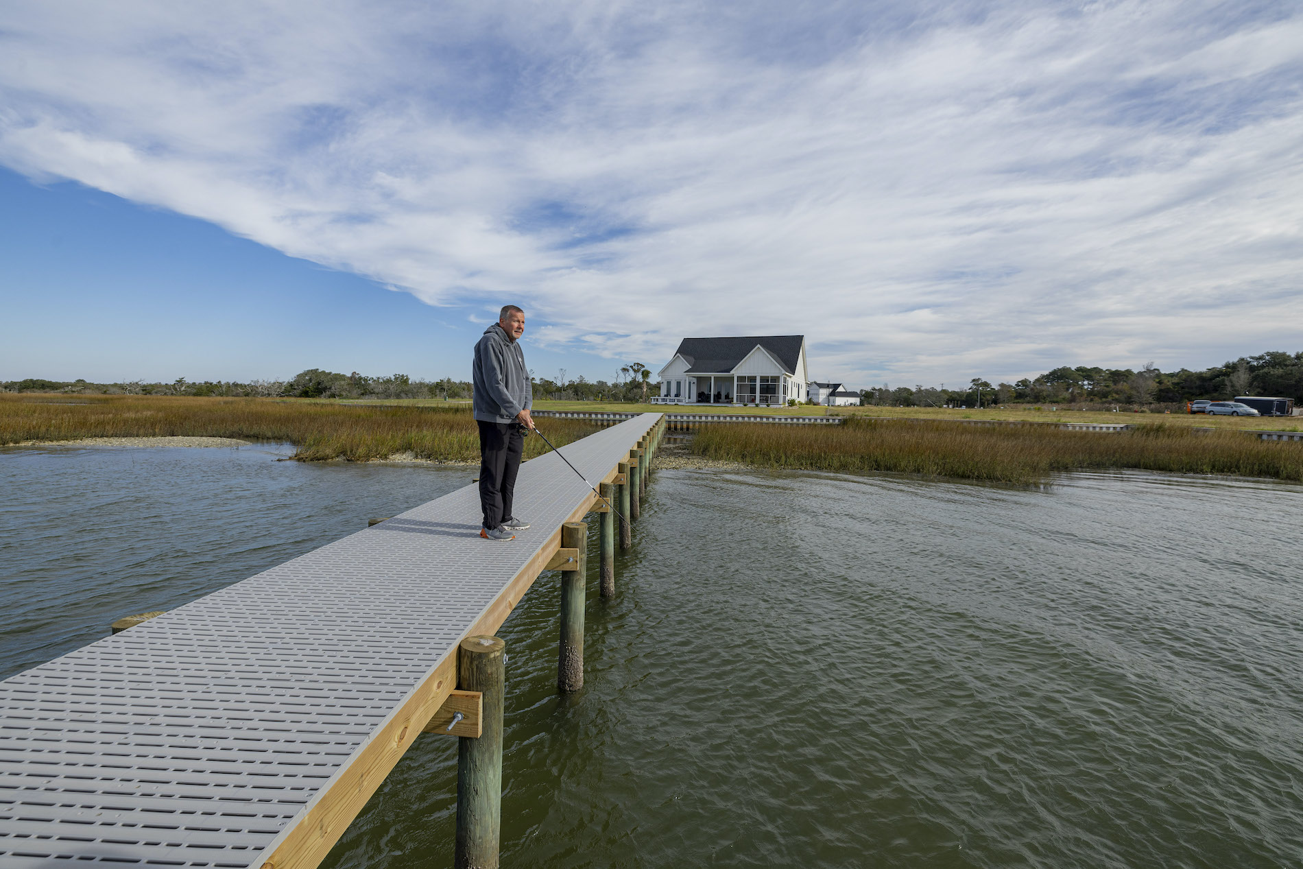 Man fishing off a wooden framed pier with Titan classic decking. Blue skies and a white house in the background.