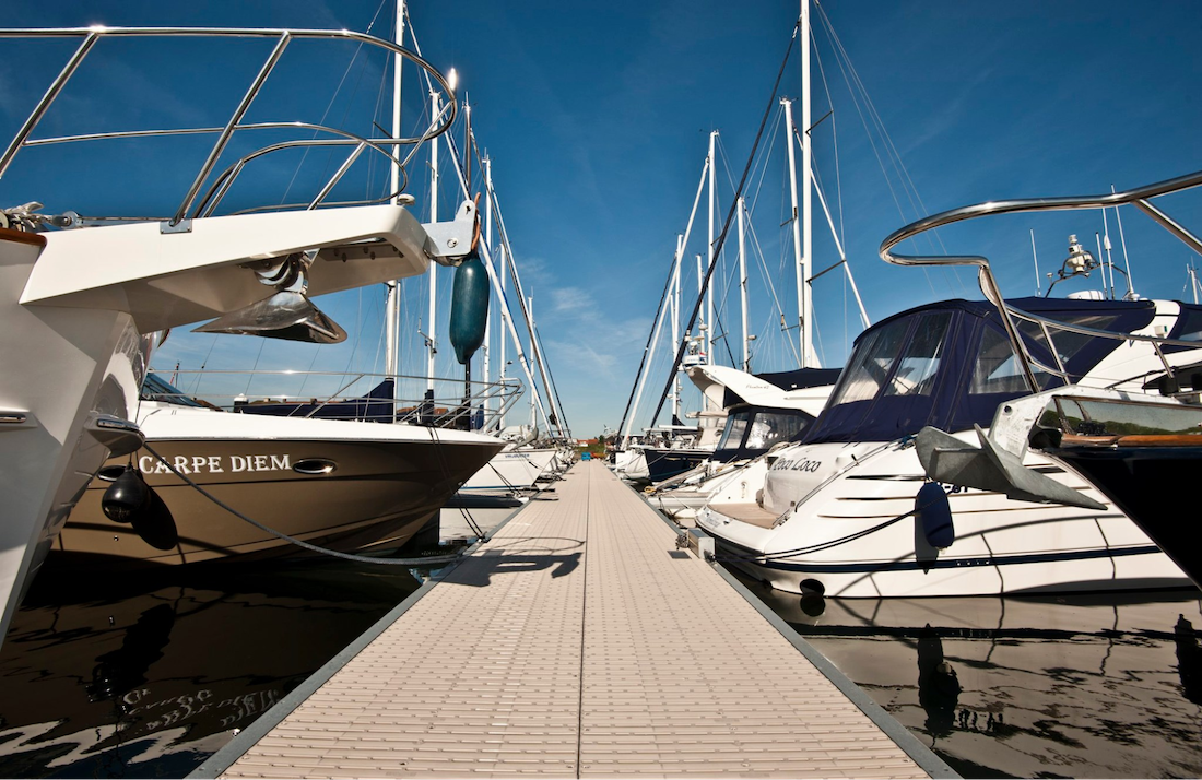 Various boats are docked at a marina. The dock is made out of polypropylene deck boards.
