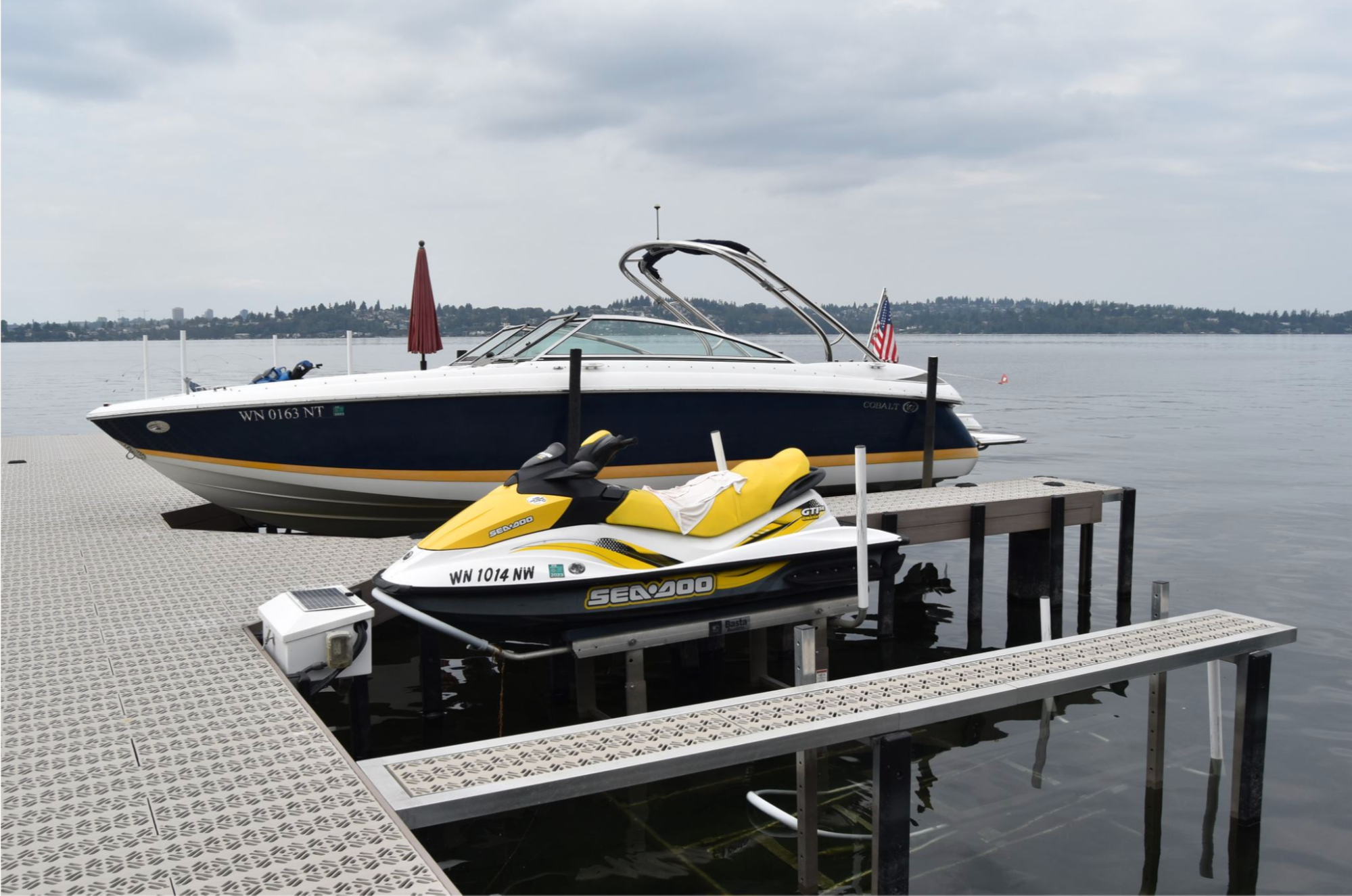 A black and white boat and a yellow jet ski are docked and on lifts to raise them from the water.