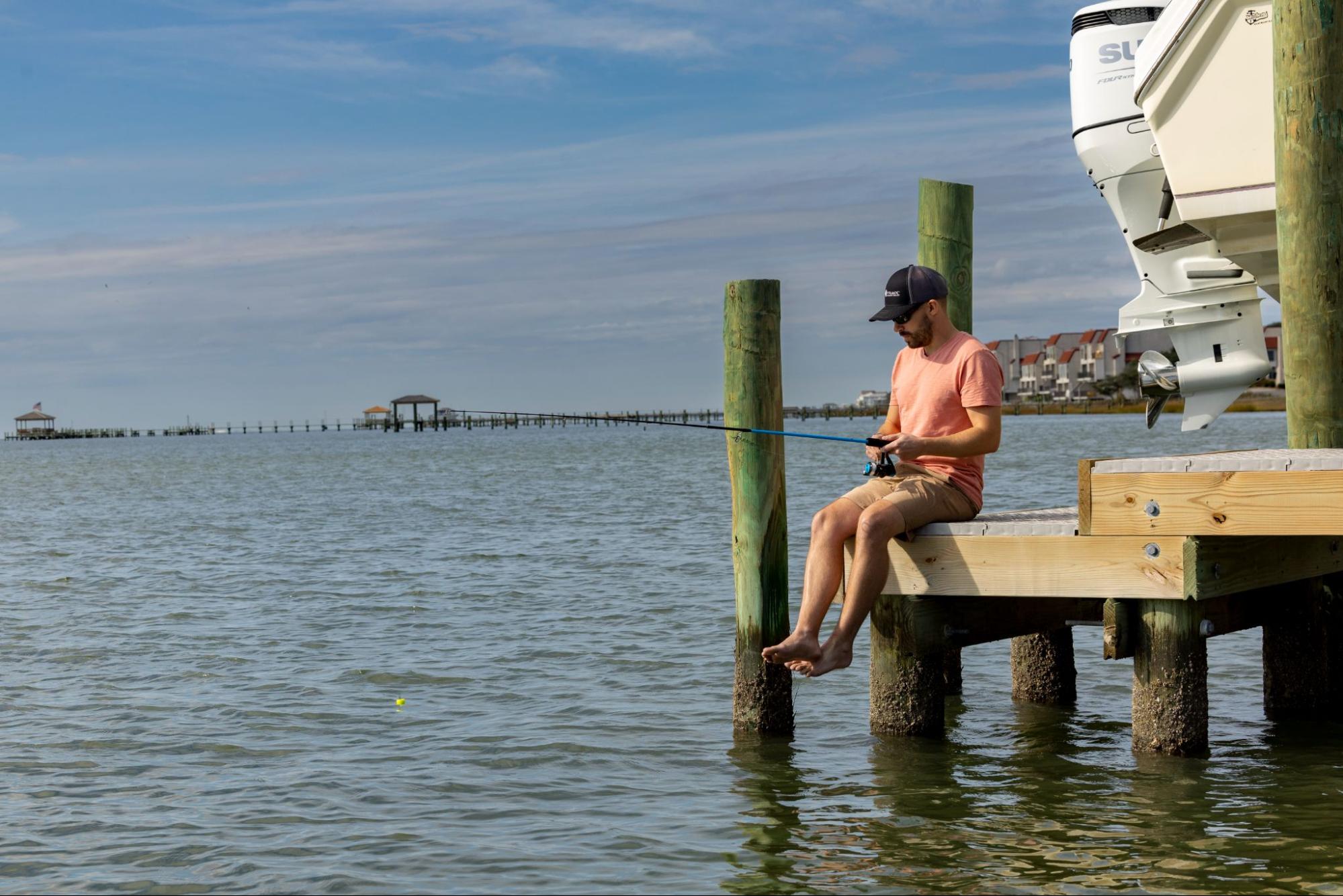 A man swings his legs off a lower portion of a dock using Titan Decking marine decking with a fishing pole.