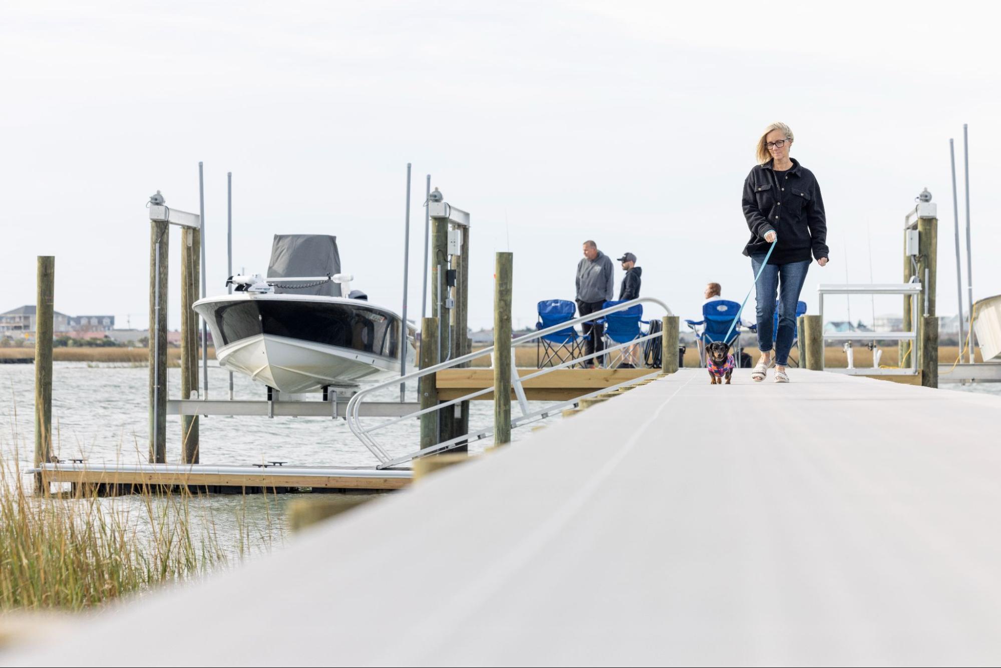 A woman walks her dog on her marine deck with Titan Decking marine deck material. On her right is a ramp leading down to the water with accessibility rails.