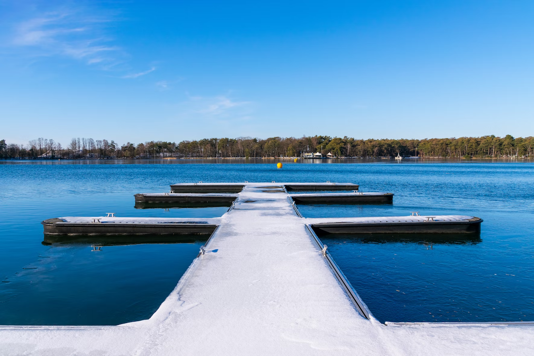 The view down the middle of a dock, with smaller docks connected on either side. The docks are covered in a light coating of snow. 