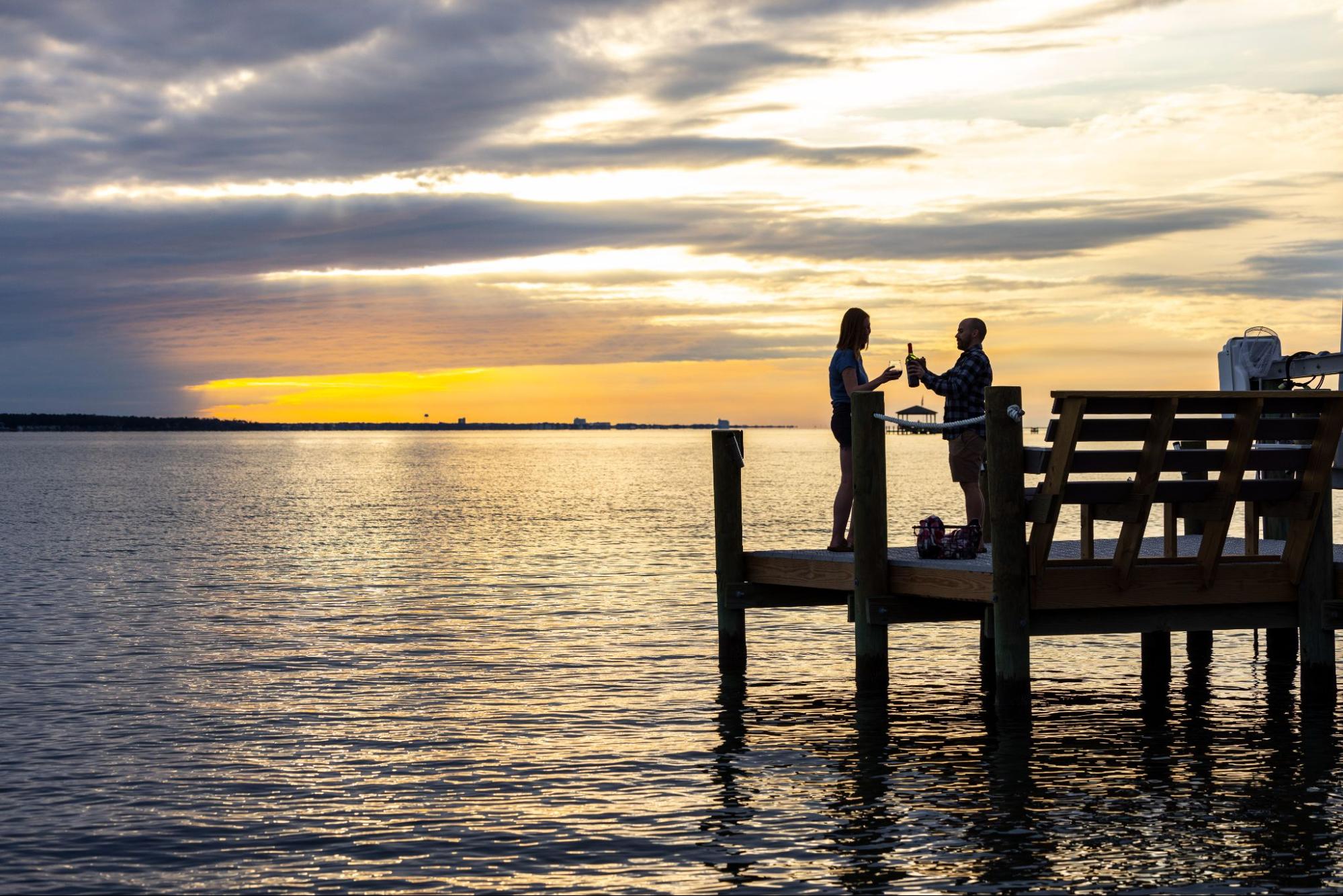 A couple shares a bottle of wine on a dock with Marine Titan decking overlooking a sunset.