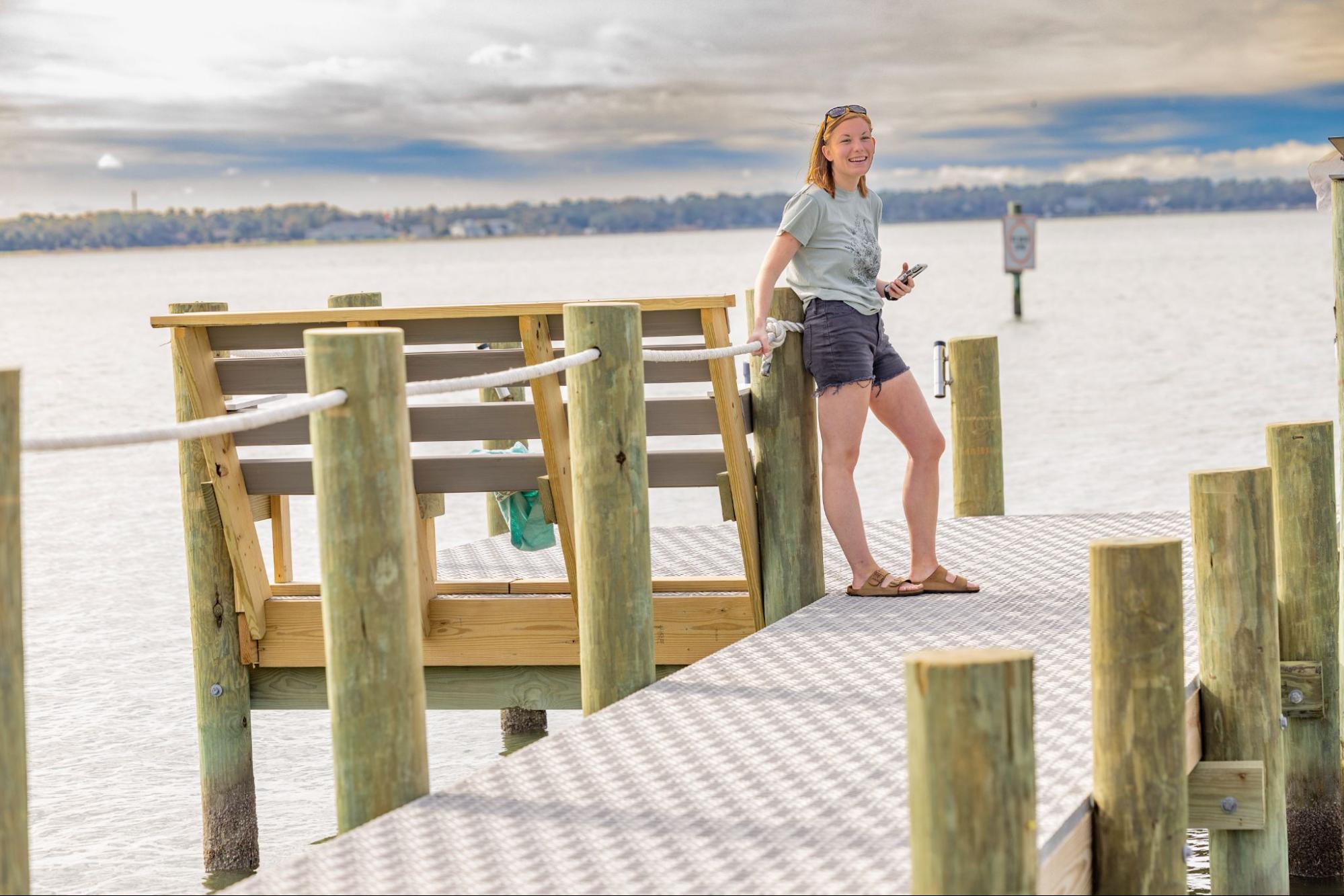 A woman is standing on a dock with Titan Decking marine decking and is resting her hand on a white rope connecting the dock beams.