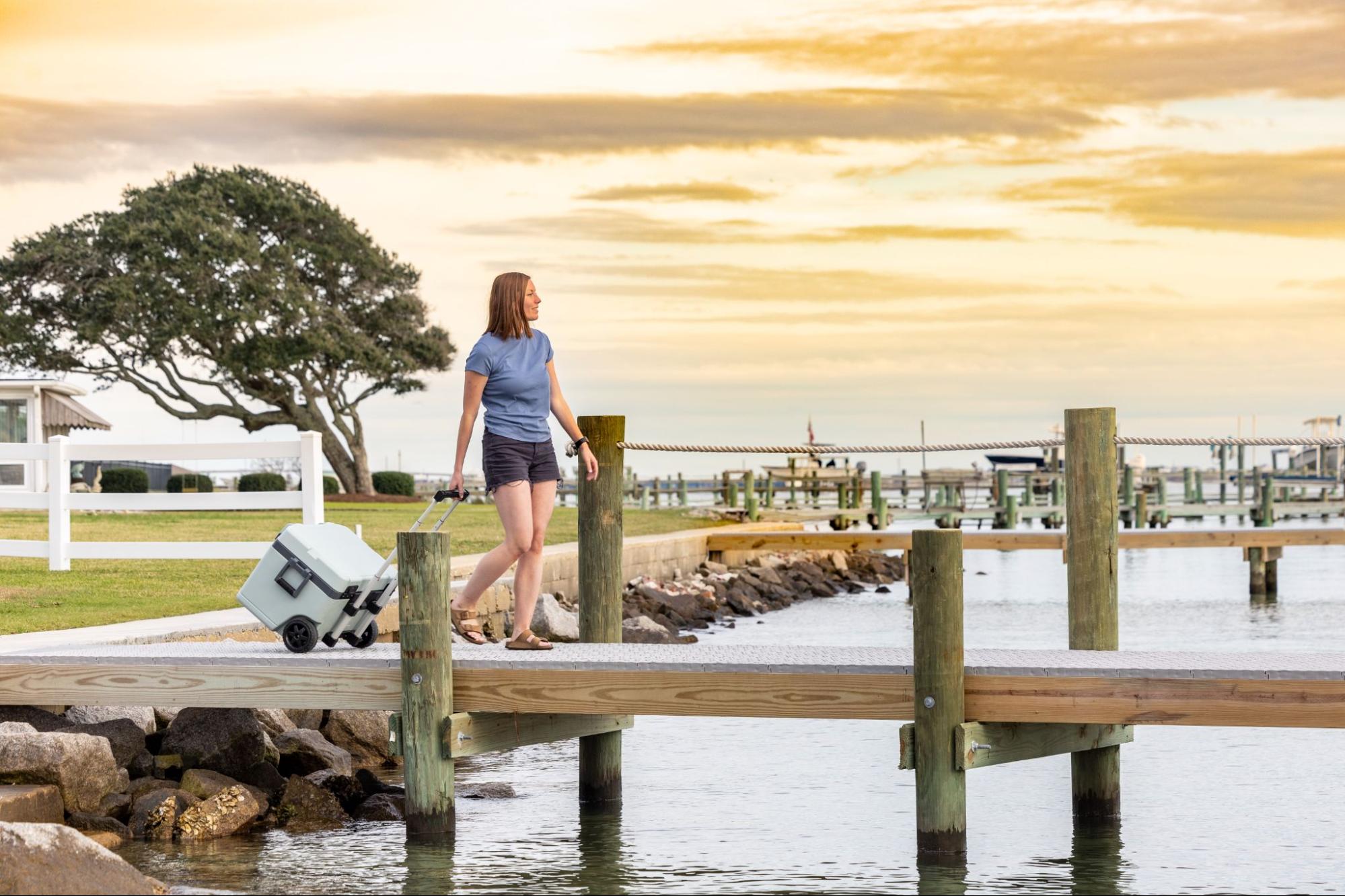 A woman is rolling a cooler on a dock over water that has Titan Decking marine decking material on it.