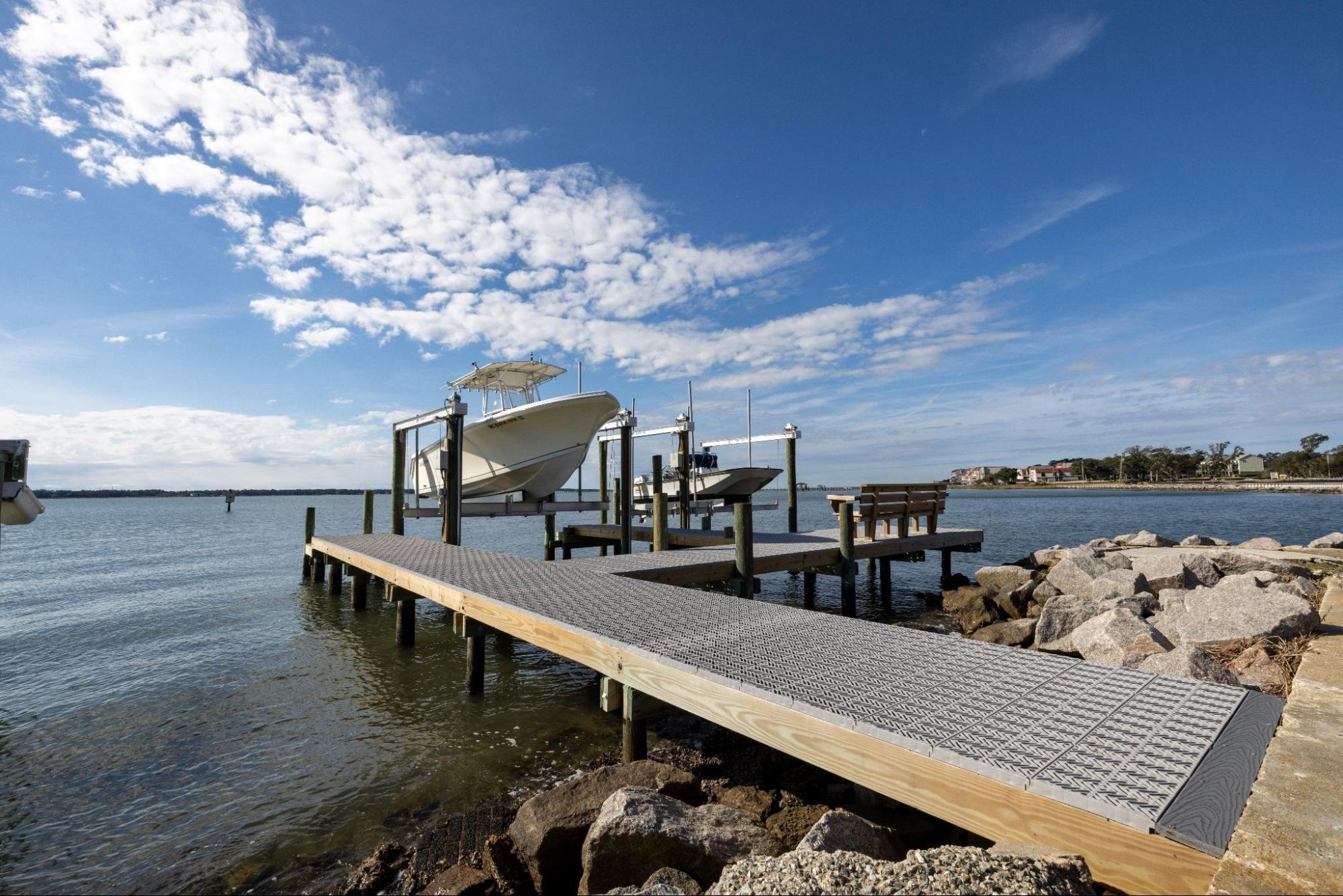  The start of a dock with Titan Decking marine decking material on top of rocks leading to two lifted boats at the end.