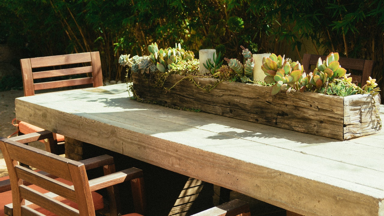 The view of a corner of an outdoor, rustic dining table. There is a succulent centerpiece in a wood box and two chairs.