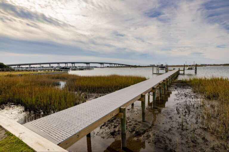 A wooden framed dock with Titan Deck classic boards extends over a marsh on a cloudy day.