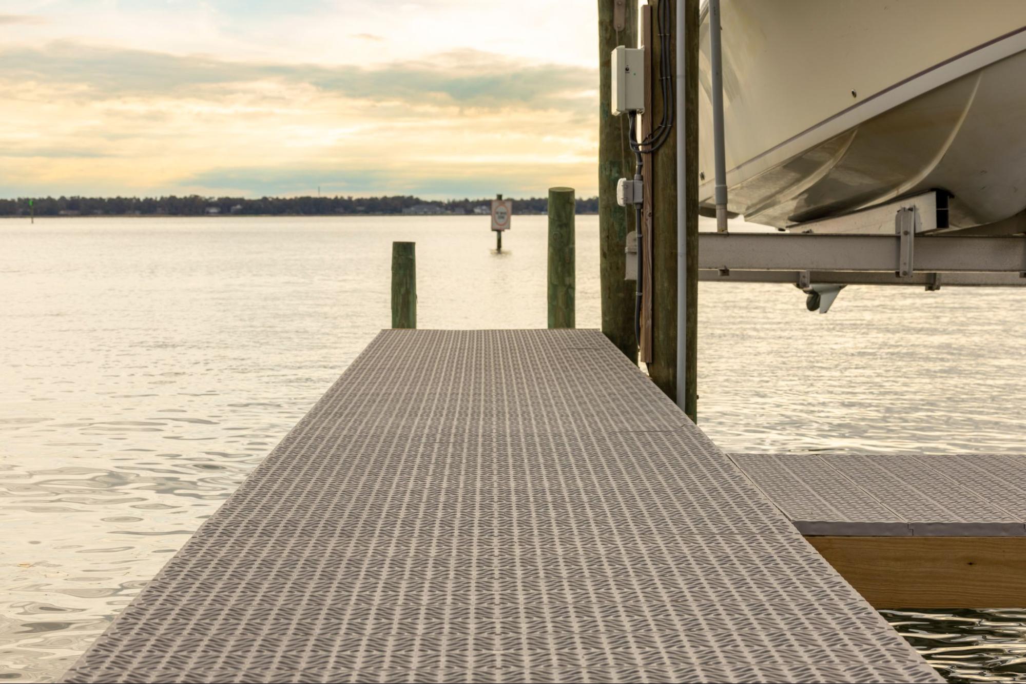 Titan Deck decking is pictured. The sun is setting in the background, and there is a boat on a lift in the top right corner.