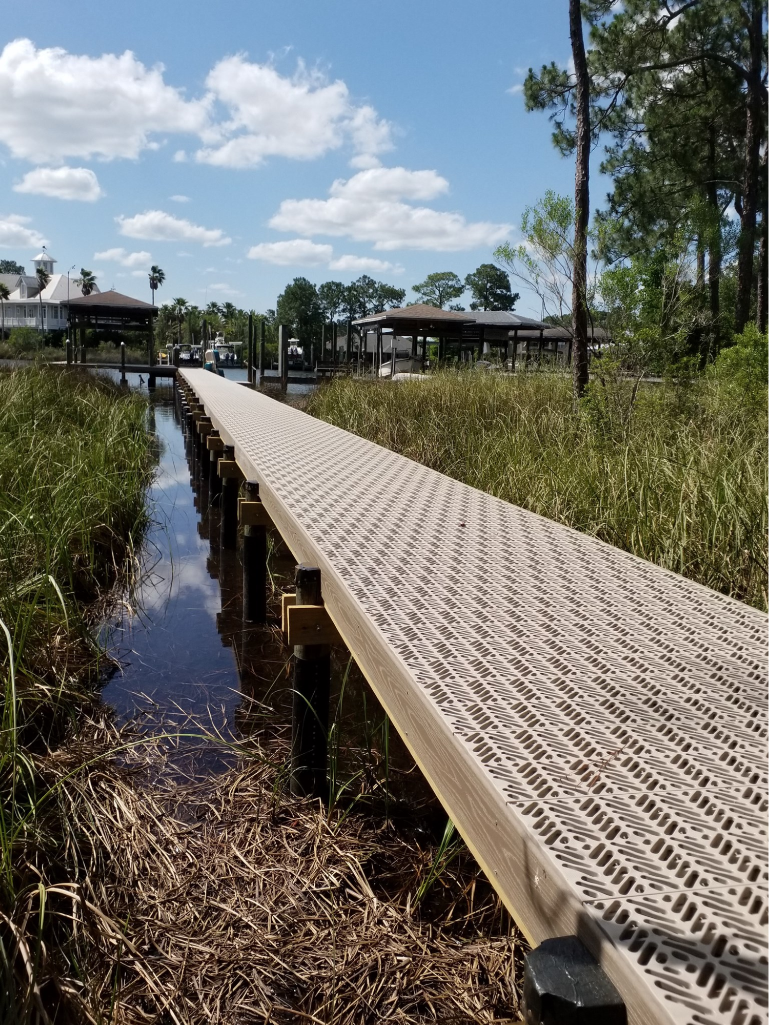 A long deck leading down to multiple gazebos. The dock is surrounded on either side by water and grasslands.