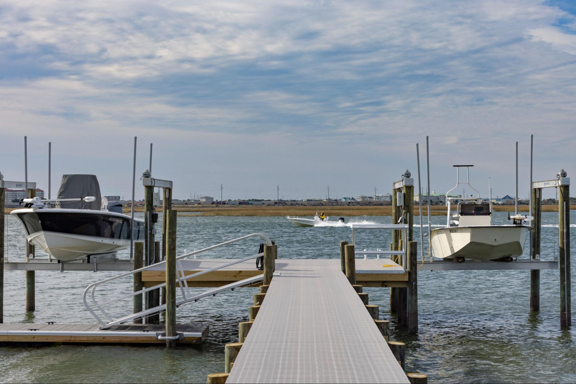 The photo depicts a T-shaped dock with two boats lifted by a boat lift on each side. The boat on the left-hand side is larger than the boat on the right-hand side. 