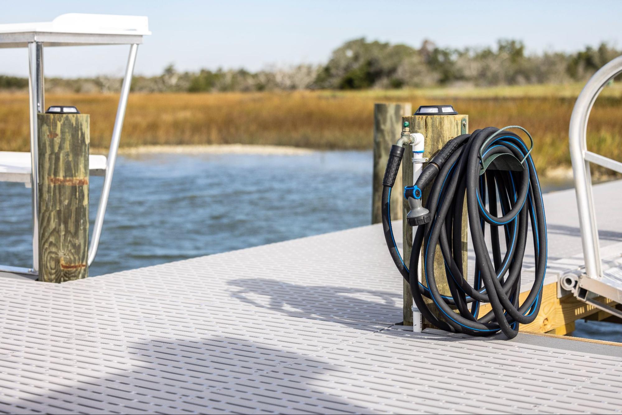 The photo depicts a dock with a body of water and a marsh in the background. In the foreground, there is a black, coiled-up hose. 