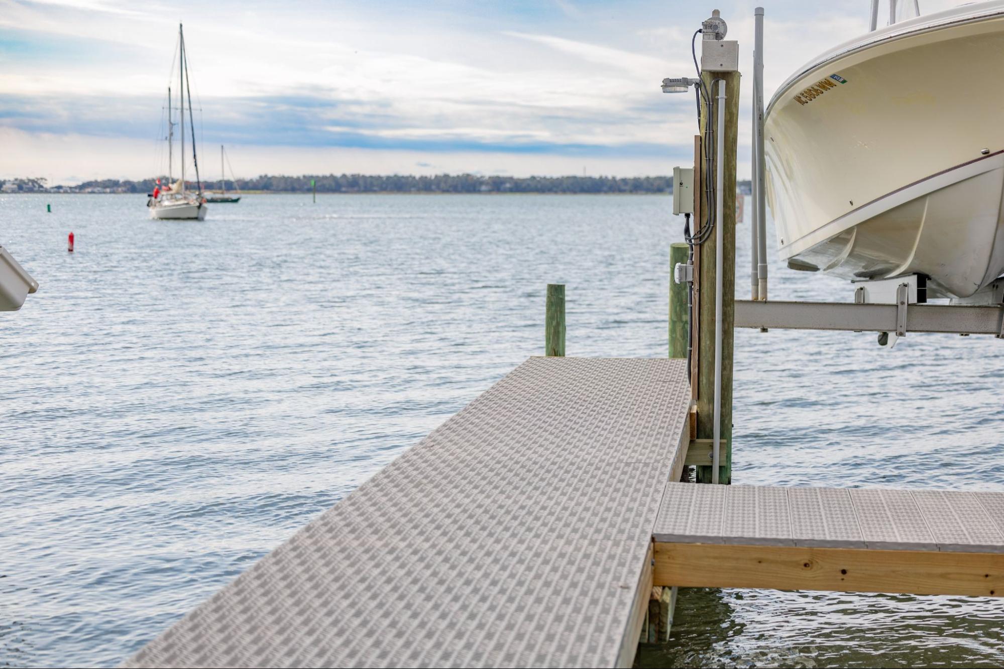 The photo depicts a dock with a boat lift. There are two sailboats on the horizon line. 