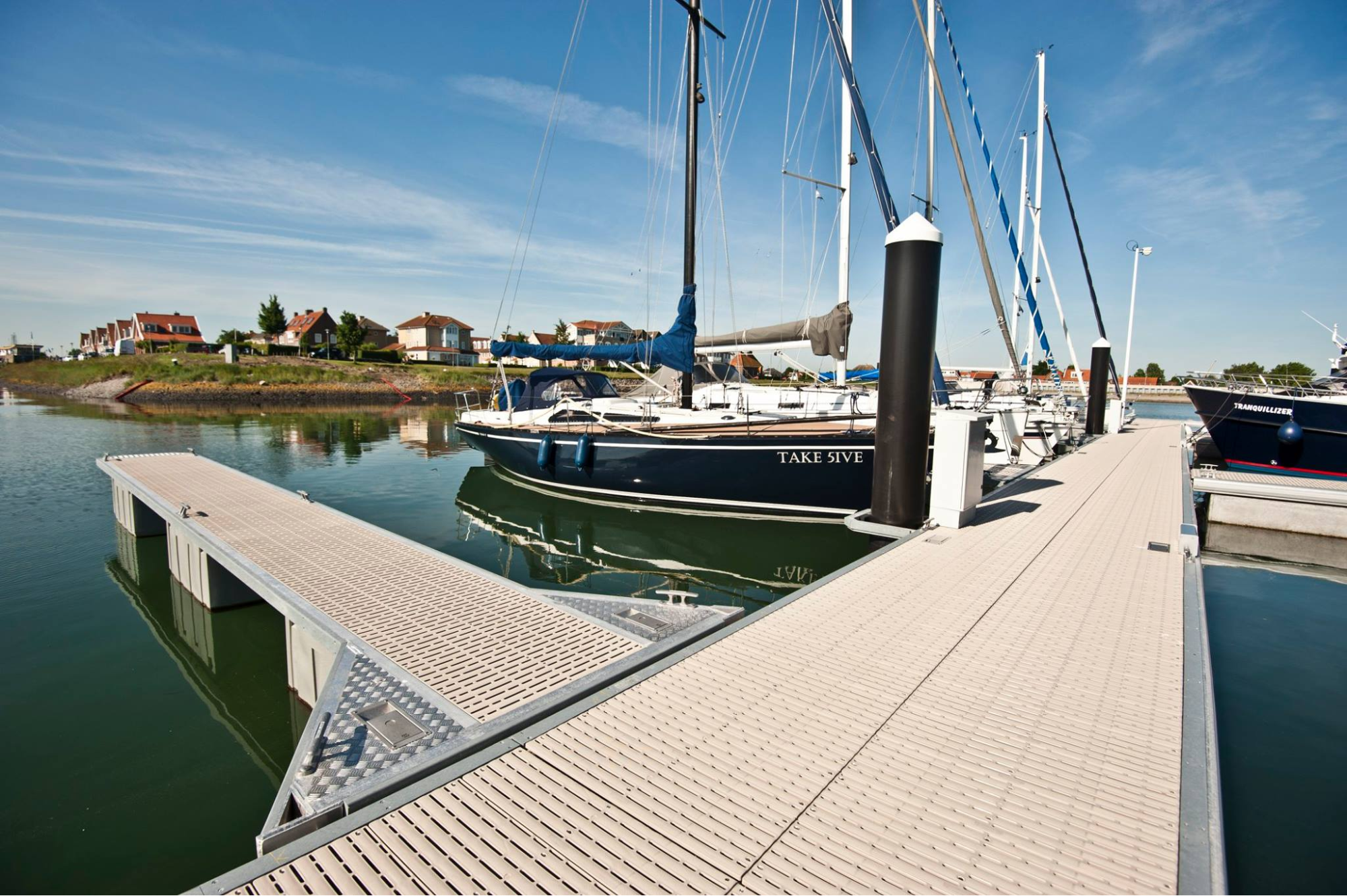 The view down a dock with a side dock protruding from the side. There are multiple boats docked up to the main pier. 