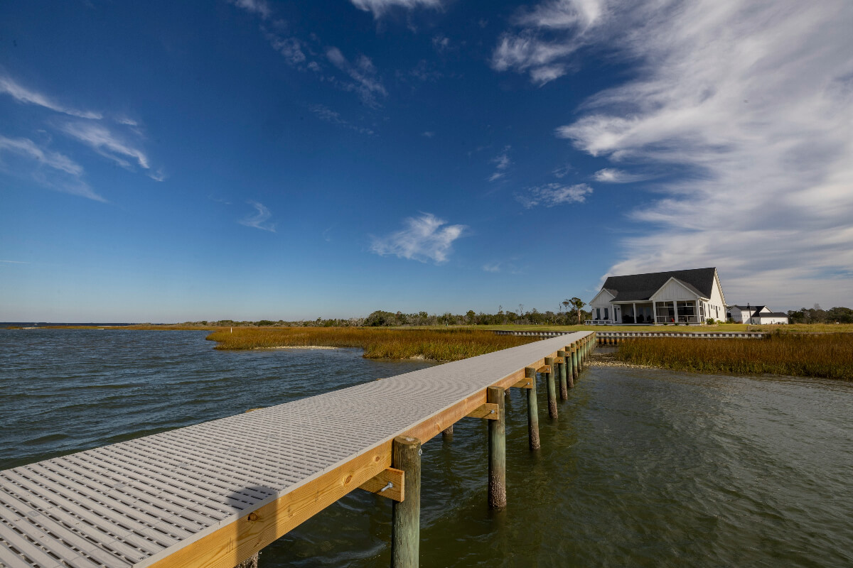 A white house has a long Titan Deck dock that extends into the water. 