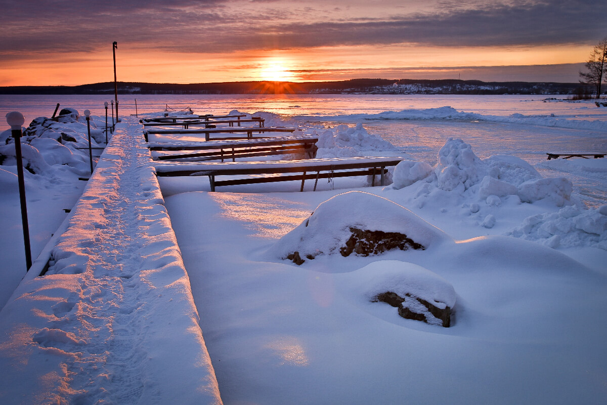 A dock is covered with snow during a sunset. 